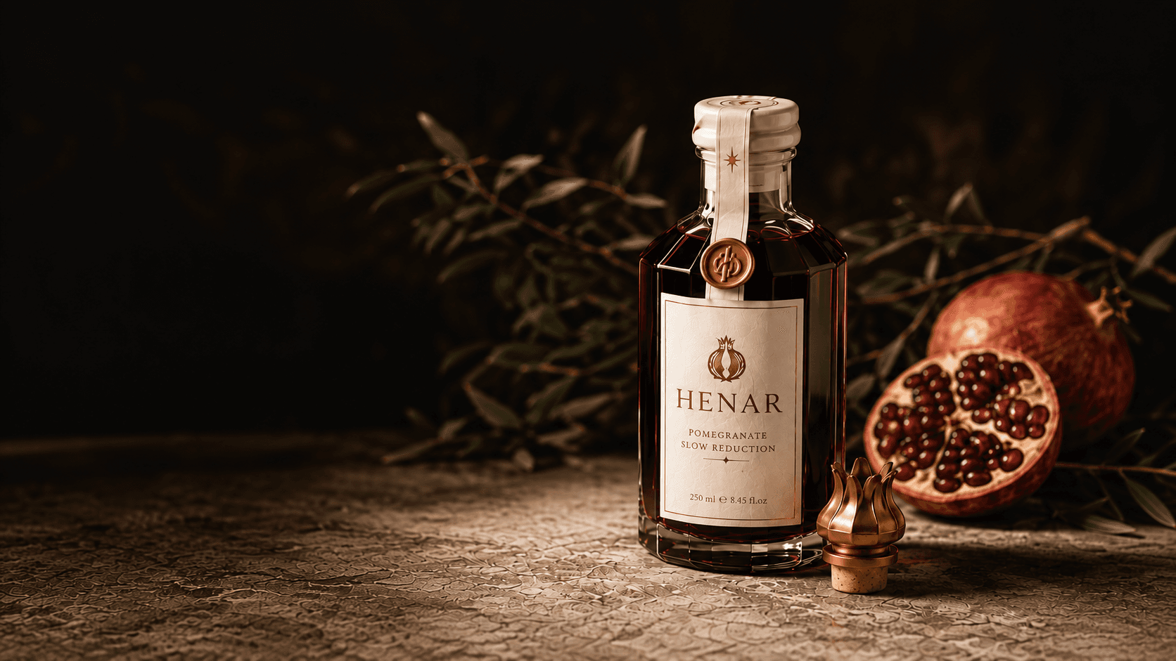 A bottle of Henar Pomegranate Slow Reduction beside a halved pomegranate